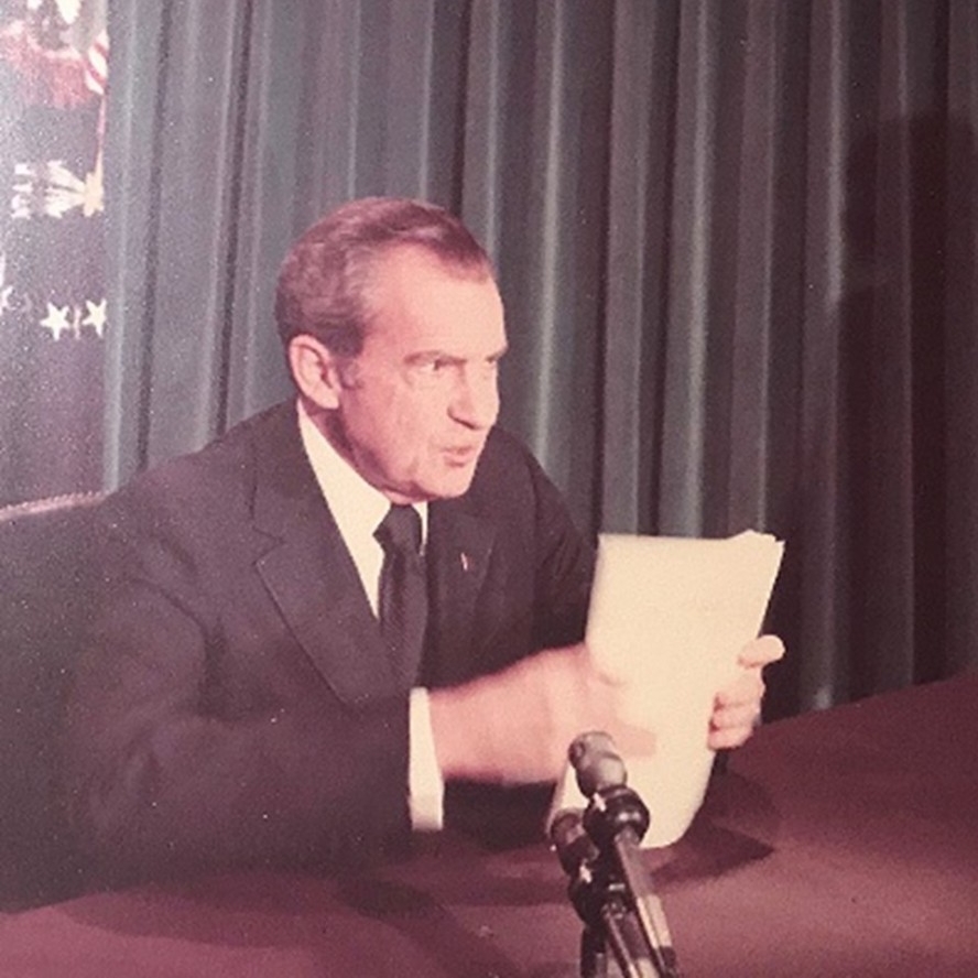 Richard Nixon speaking into a microphone while holding a paper